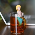 Detailed close-up of a mermaid silicone tea infuser hanging on a glass cup - Mermaid-Yellow