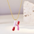 Detail of pink and red enamel letter H pendant on a golden chain necklace - Letter H