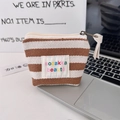 Close-up of striped canvas small makeup bag with brand label on a laptop keyboard - 1.5cm Striped Brown