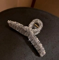 Detailed close-up of a pearl shark hair claw clip with rhinestones on a black tray - Clear