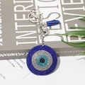Blauer Evil Eye Schlüsselanhänger mit Strass und Lederquaste auf minimalistischem Hintergrund - Dunkelblau