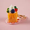 Mini-Obstkuchen Schlüsselanhänger mit Beeren- und Sahnedetails auf rosa Hintergrund - Orangencreme mit goldenem Schlüsselring