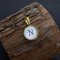 Golden pendant with letter N on white shell inlay, resting on a wooden slice - Letter N / 17x20mm