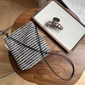 Vista plana de un bolso bandolera de tweed a rayas sobre una mesa de madera y accesorios - Tejido a Rayas Blancas y Negras