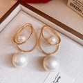 Detailed close-up of golden cross-hoop earrings featuring large white pearls on a wood tray - White Pearl Style / White
