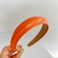 Close-up of hand holding an orange faux leather padded headband with smooth texture - Orange