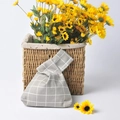 Close-up of Japanese knot bag in grey plaid linen leaning against a sunflower basket - Grey Grid