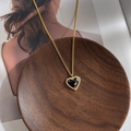 Close-up of golden necklace with black heart pendant on a decorative wooden tray - Vintage Black Heart Necklace