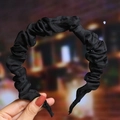 Detail view of a black pleated fabric headband held by hand with soft night background - Black (Cloth Pleated)