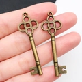 Ciondoli chiave a forma di cuore in bronzo vintage mostrati sulle dita per misura - Chiave in Bronzo Antico 15x47mm