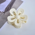 Top view of a creamy white flower hair claw clip on a clean surface with a magazine - Cream