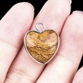 Handheld heart-shaped agate pendant with silver metal frame and brown wood grain stone - Picture Jasper Silver Edging