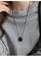 Close-up of a minimalist black oval pendant necklace worn on a grey textured shirt - Black