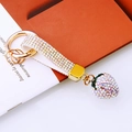 Macro shot of colorful rhinestone strawberry keychain with gold plated link on book - White