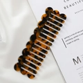 Wavy tortoise shell acetate comb with wide teeth on white silk and magazine background - Tortoise