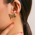 Polished gold bow earrings with ribbon texture worn by a model in a close-up view - Textured Plated Bow Stud Earrings / Gold