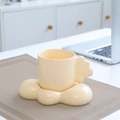 Cream ceramic coffee mug with cloud handle and matching saucer set on a woven mat - Cloud Cup & Saucer - Apricot
