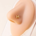 Close-up of gold letter M nose stud with zircon micro-paving on a model's nose - Letter M / Gold