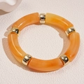 Minimalist acrylic bracelet with amber tubes and golden beads on a white board - Yellow