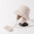 Detail view of winter ear-flaps bucket hat in cream faux fur with plush pom-pom ties - M (56-58cm) / Off White