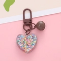 Macro shot of heart-shaped acrylic keychain filled with iridescent beads and brown bell - Brown