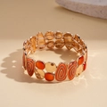 Dettaglio di un bracciale elastico dorato con smalto arancione e trame a spirale - Rosso