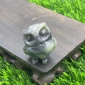 Green natural stone owl figurine on wood base with a garden grass background - Labradorite
