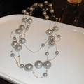 Detailed shot of layered pearl and gold-plated chain necklace on white ceramic tray - Gray