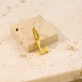 Detail of a polished gold letter L pendant resting on a natural beige stone surface - Letter-L / Steel
