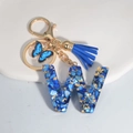 Blue resin initial W keychain with blue shell pieces, gold foil, tassel, and butterfly charm - Letter W