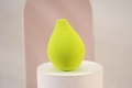 Pear-shaped yellow-green makeup sponge on a white stand with a soft geometric background - Yellow Green Pear