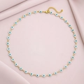 Detail of gold chain necklace featuring small evil eye charms on pink fabric background - White Green