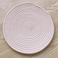 Handwoven round cotton rope placemat in light pink on a minimalist wooden background - Rice Pink