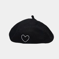 Detalle de una boina de lana negra con bordado de corazón blanco sobre una superficie plana - Negro