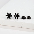 Close-up of minimalist black snowflake stud earrings with matching metal butterfly backs - Snowflake / Black
