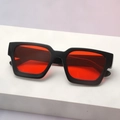 Detail view of bold black square frame sunglasses with vibrant red lenses on a white pedestal - Black Frame Red Lens