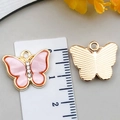 Pendentif papillon rose en acrylique avec cadre doré et cristaux à côté d'une règle - Rose Clair
