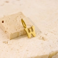 Detailed macro view of a gold W-shaped pendant on natural beige stone texture - Letter-W / Steel
