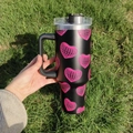 Close-up of 40oz black insulated car mug with pink disco heart patterns on grass - Pink Disco Heart