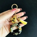 Detailed view of resin letter keychain with dried flowers, gold bee charm and yellow tassel - Letter O