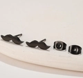 Macro shot of black matte mustache studs with backings on a white textured surface - 679 Black (Mustache)