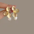 Pendientes de pétalos dorados con perla barroca colgante en elegante exhibición - Pendientes de Pétalo y Perla