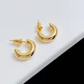 Vue macro de boucles d'oreilles créoles dorées en C sur un support géométrique blanc - Doré