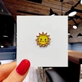 Close-up of cute yellow and orange sun enamel pin on white card held by a hand - 17*Sun Smile Pin