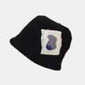 Detailed close-up of thick knit black bucket hat with abstract geometric patch - Black