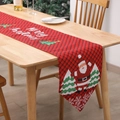 Red plaid Christmas table runner with Santa Claus and trees on light wooden dining table - Santa Claus