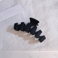 Dettaglio di un fermaglio nero opaco a onde geometriche su uno sfondo bianco strutturato - Nero