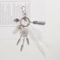 Macro detail of dreamcatcher keychain with Hamsa hand and real white feather charms - White