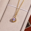 Detailed close-up of a golden necklace featuring a round purple gemstone pendant in a jewelry box - October Pink