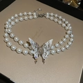 Détail d'un collier de perles double épaisseur avec un grand pendentif papillon scintillant sur boîte - Collier de perles papillon double couche / Argenté
